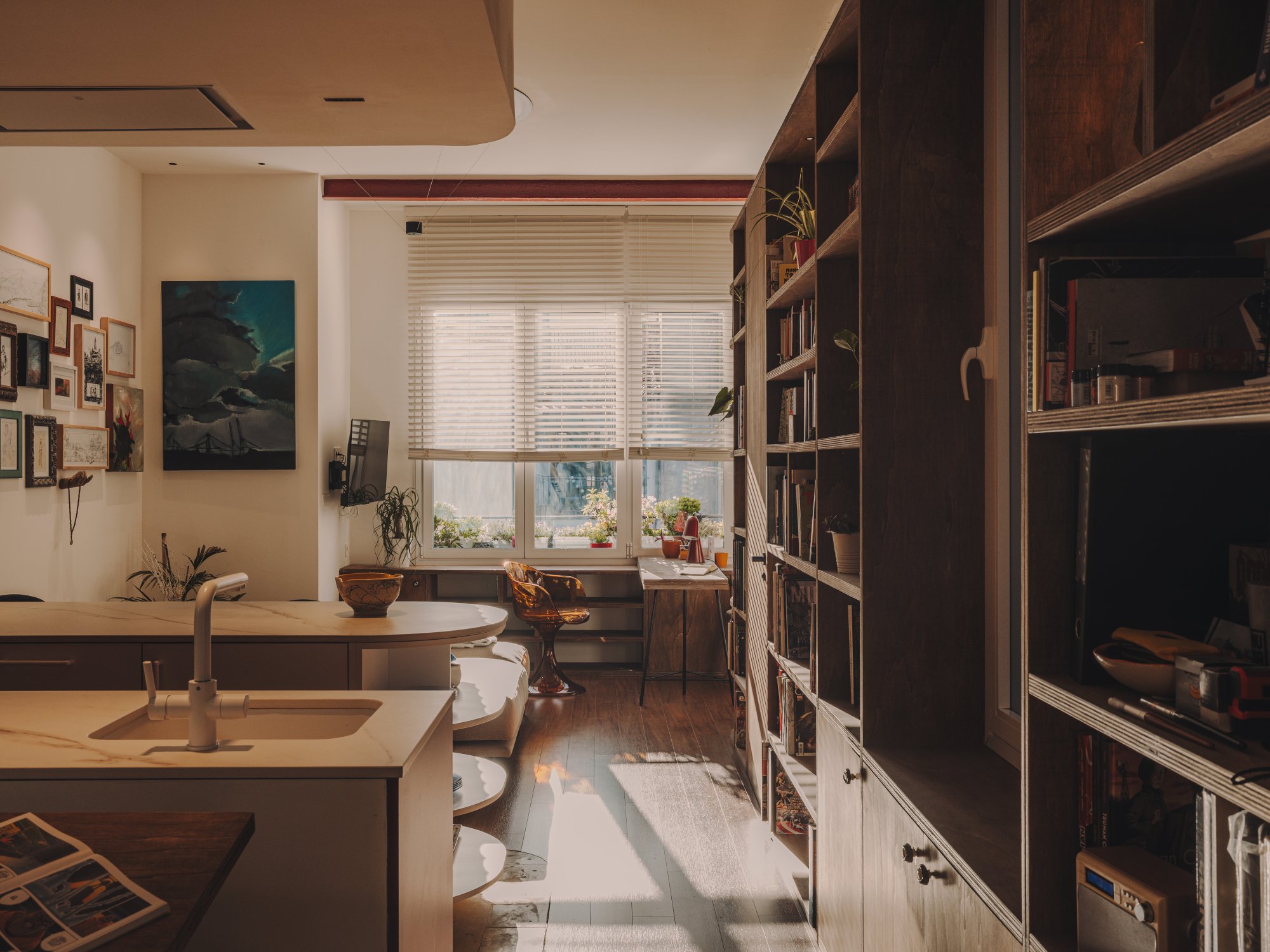 Cocina con isla y estantería junto a la ventana del salón con luz de tarde