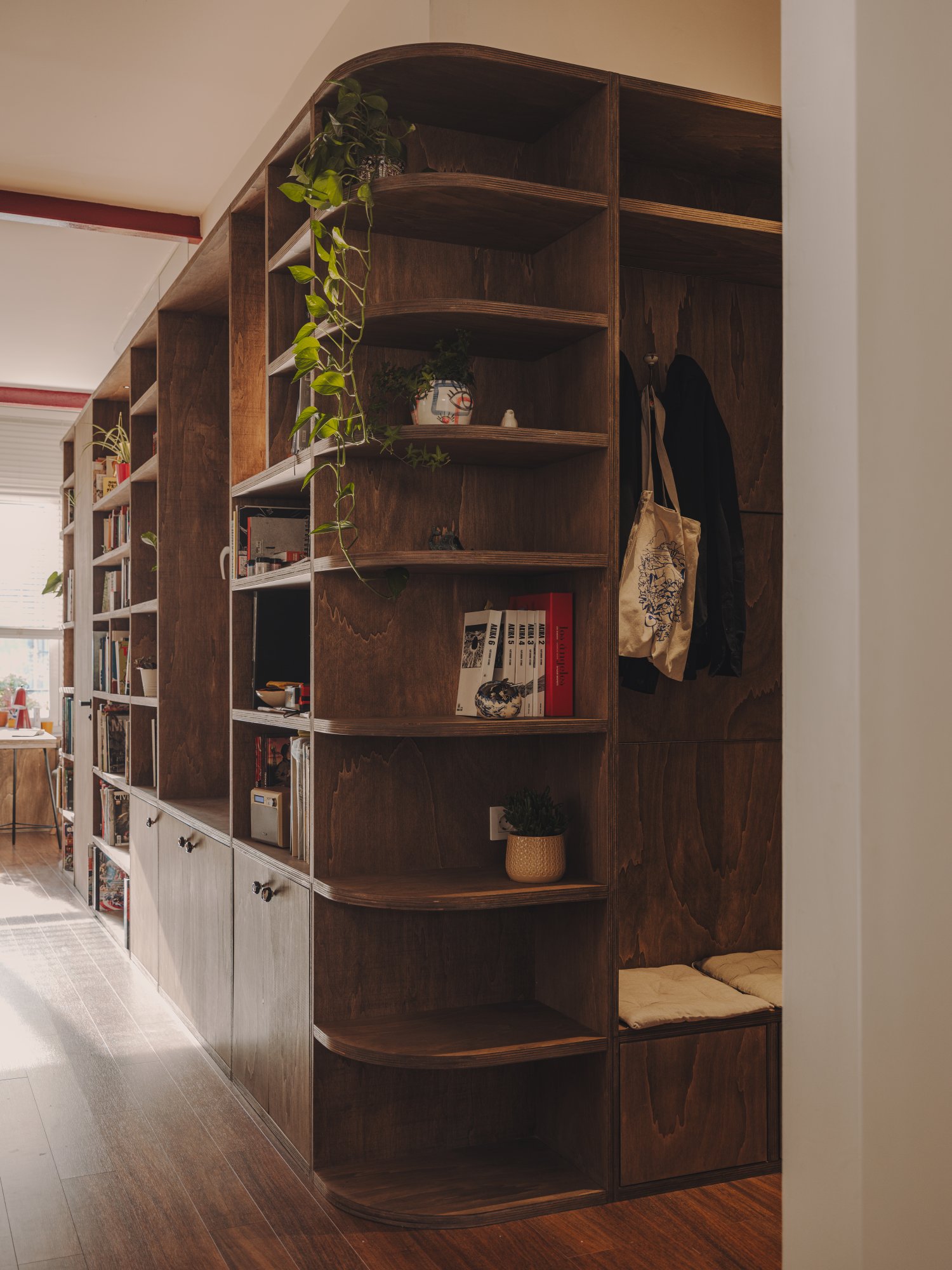 Estantería curva de madera con plantas y banco en la entrada